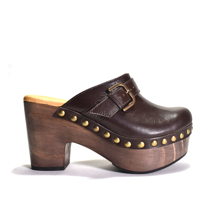 A dark brown leather clog shoe with a chunky wooden platform and block heel, decorated with brass studs and a buckle strap, shown against a plain white background.
