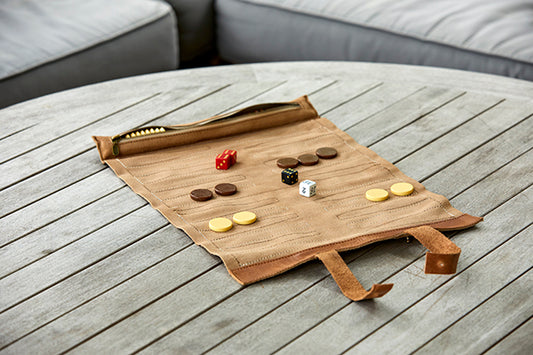 A travel backgammon set rolled up on a wooden table, with game pieces and leather trim visible.