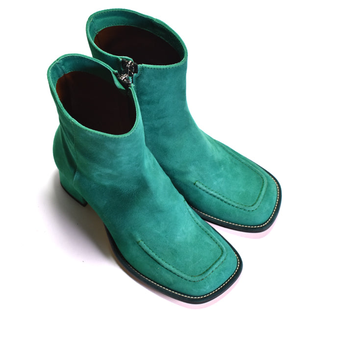 A pair of green suede ankle boots with square toes, low block heels, and side zippers, shown on a plain white background.