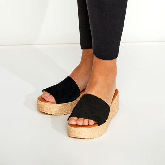Black open-toe sandals with woven soles worn by a person on a white background