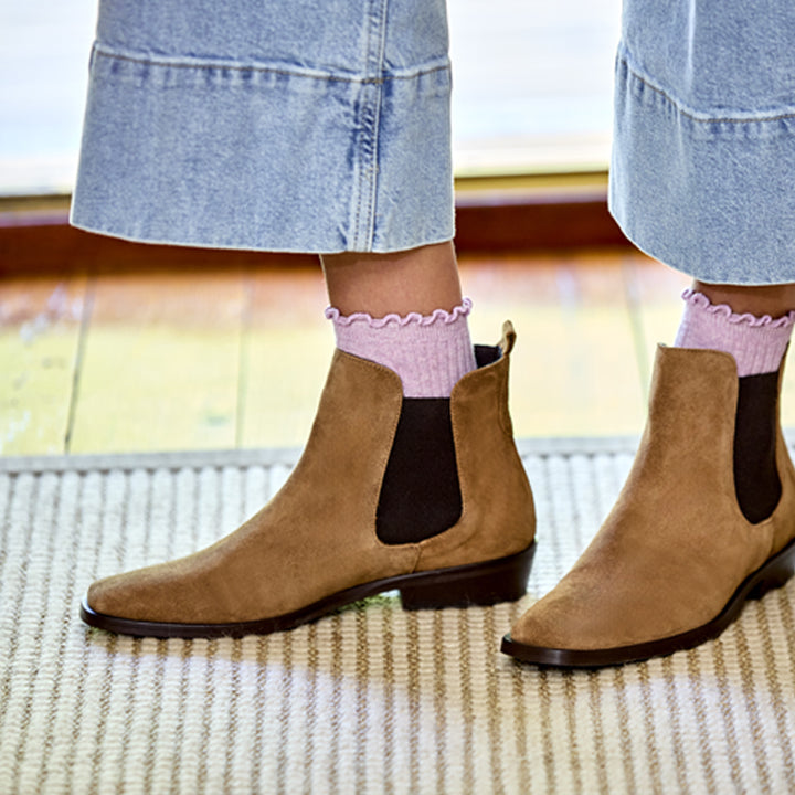 Brown ankle boots worn with light pink socks on a blurred indoor background