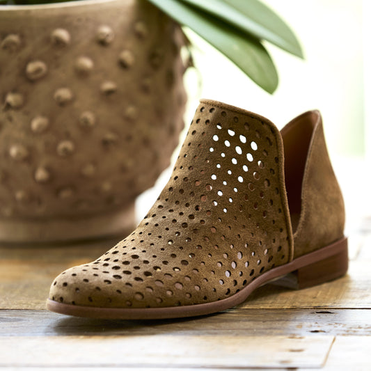 Brown perforated ankle boots on a wooden surface with a plant pot in the background