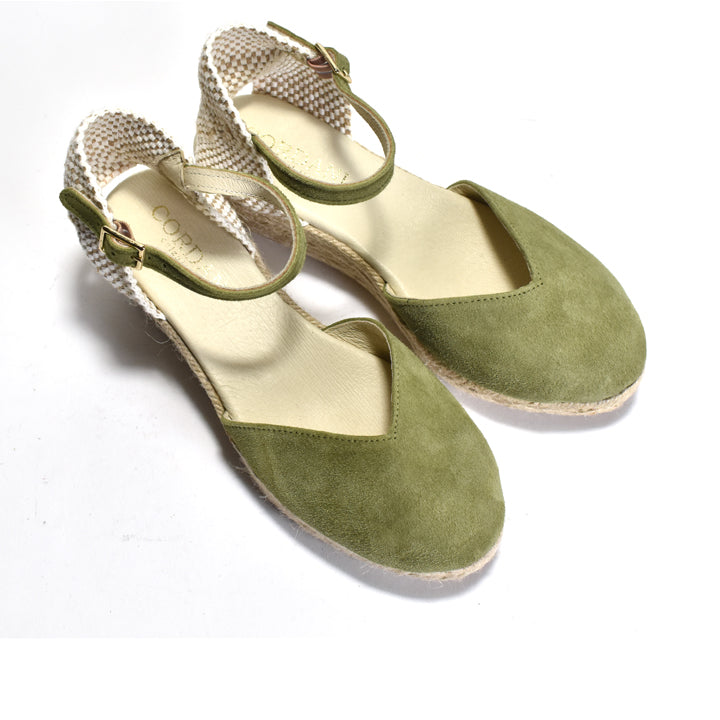 Pair of green suede shoes with woven straps on a white background