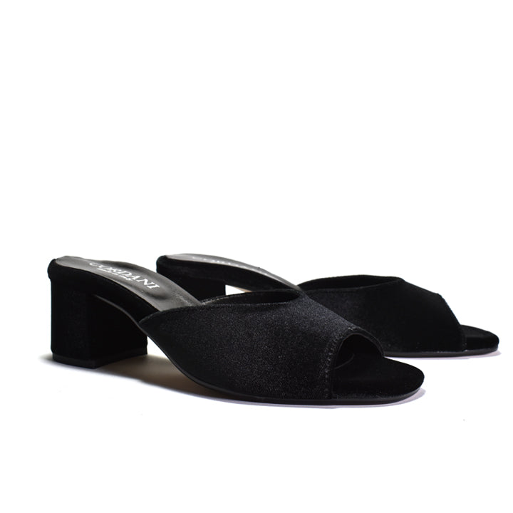 A pair of black velvet mule sandals with a block heel, shown from a three-quarters angle on a white background.