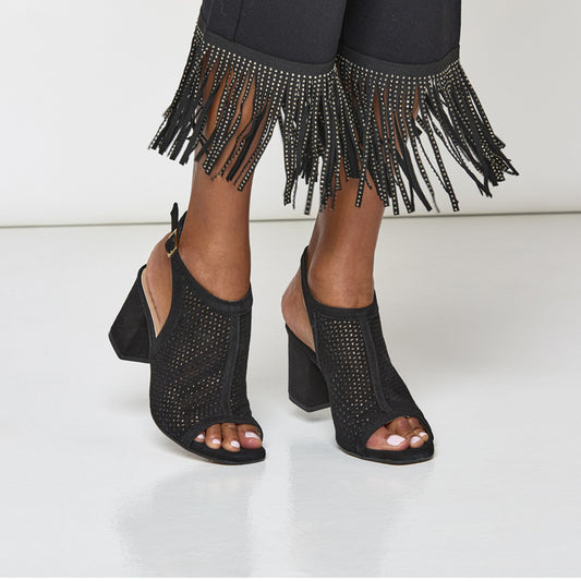 Black high-heeled shoes with open-toe design worn with black pants featuring fringe and embellishments.