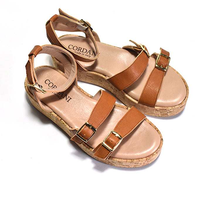 A brown two-strap sandal with adjustable metal buckles, a cork-wrapped platform, and a leather ankle strap.