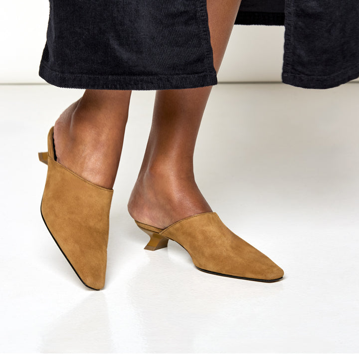 woman wearing Tan suede mules worn with black skirt on a white background
