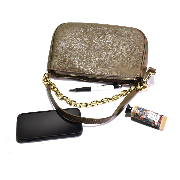 Beige handbag with chain strap, phone, pen, and tube oflotion on a white background
