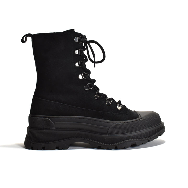 A black mid-calf lace-up boot with a thick lug sole, black suede upper, and silver metal eyelets, shown from a side profile on a white background.