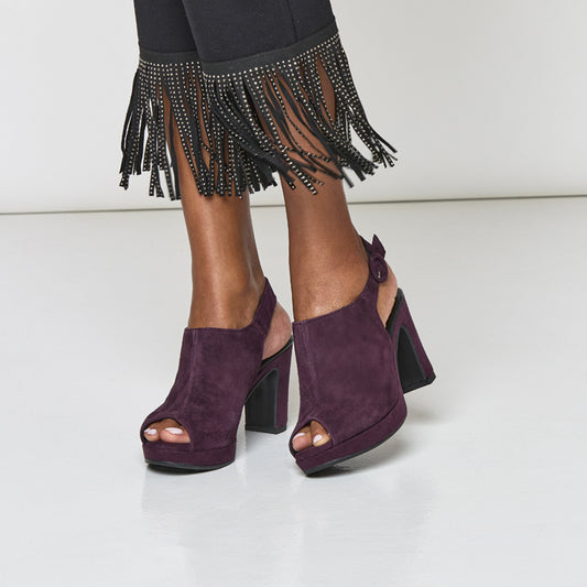 Purple open-toe high-heeled shoes worn with black pants featuring fringe details.