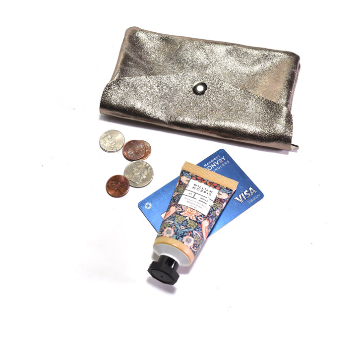 Metallic bronze wallet with coins, hand cream, and Visa card on a white background