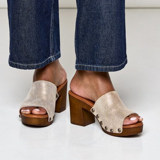 A brown pair of sandals with a shimmering lip pattern on the upper and a stud detail on the wood-like platform. The sandal has a lightly padded leather footbed and a rubber sole.