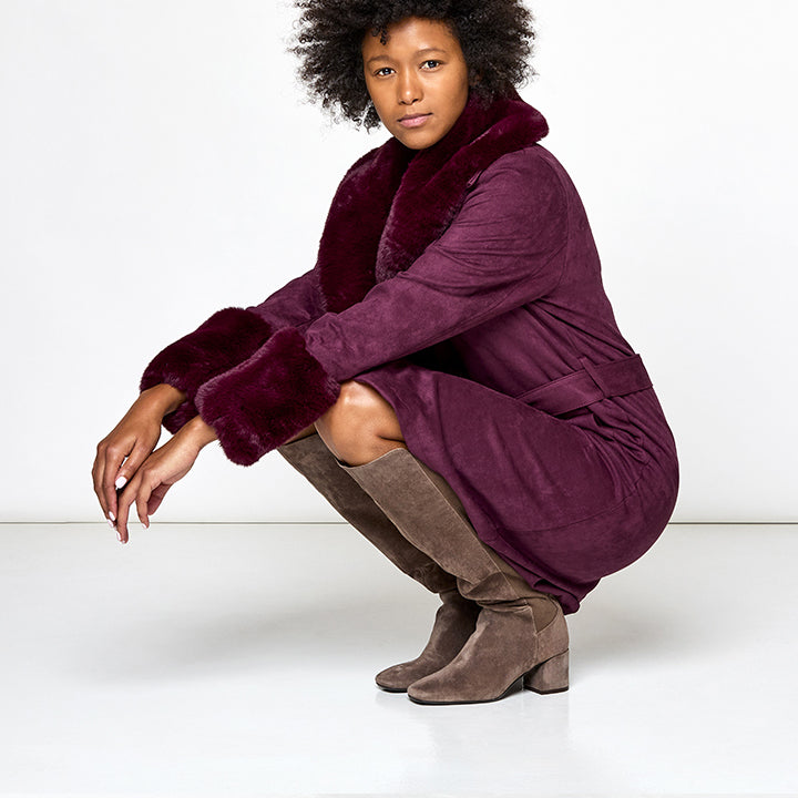 Woman wearing a purple coat and brown boots on a white background