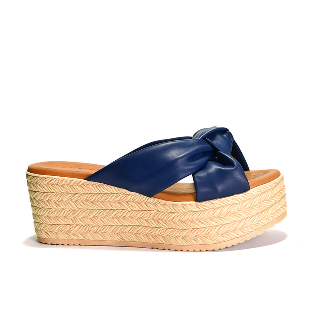 Blue sandal with a bow on a beige woven platform sole against a white background
