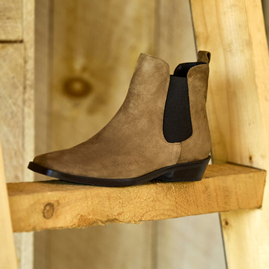 Brown Chelsea boot with black sole on a wooden shelf