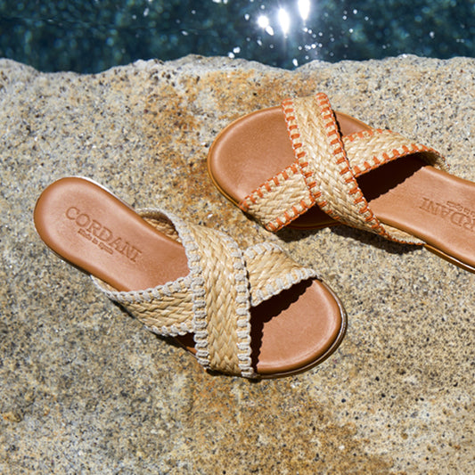 Pair of sandals with woven straps on a stone surface near water.
