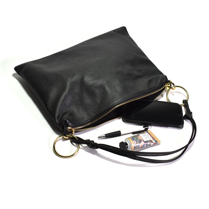 A black pebbled leather clutch bag with gold-tone hardware, shown open with a black smartphone, pen, tube of cream on a white background.
