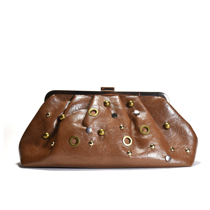 A brown leather clutch bag with a pleated design, adorned with gold and silver studs, grommets, and metallic accents, set against a plain white background.