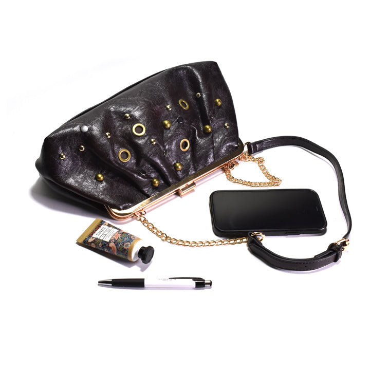 A dark brown leather kiss-lock handbag with gold-tone hardware, shown with a gold chain strap, a black phone case, a small tube of hand cream, and a pen on a plain white background.