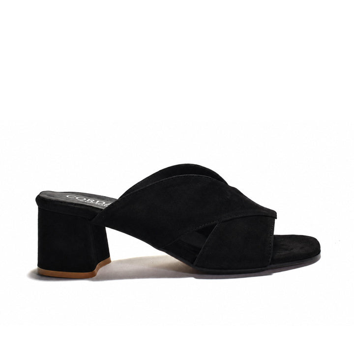 A black suede mule sandal with a block heel and crisscrossing straps, shown from a side profile on a white background.