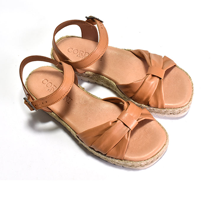 A brown nappa leather sandal with a woven rafia wrapped wedge, leather lining, and an adjustable buckle strap on a white background.