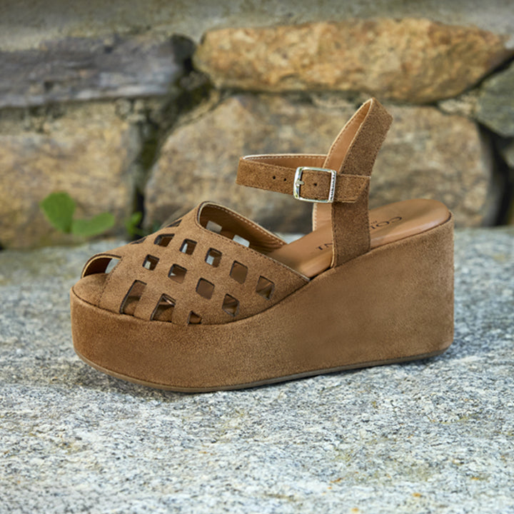 Brown suede wedge sandal on a stone surface with rocks in the background