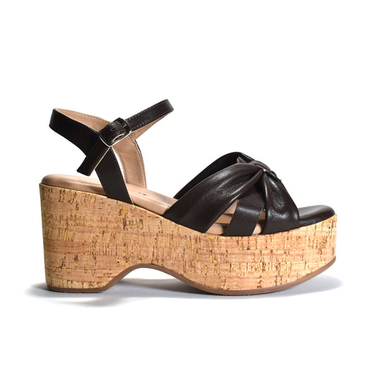 A single black leather platform sandal with an ankle strap and crisscross front straps, featuring a thick cork-wrapped wedge heel, shown from a side profile on a white background.