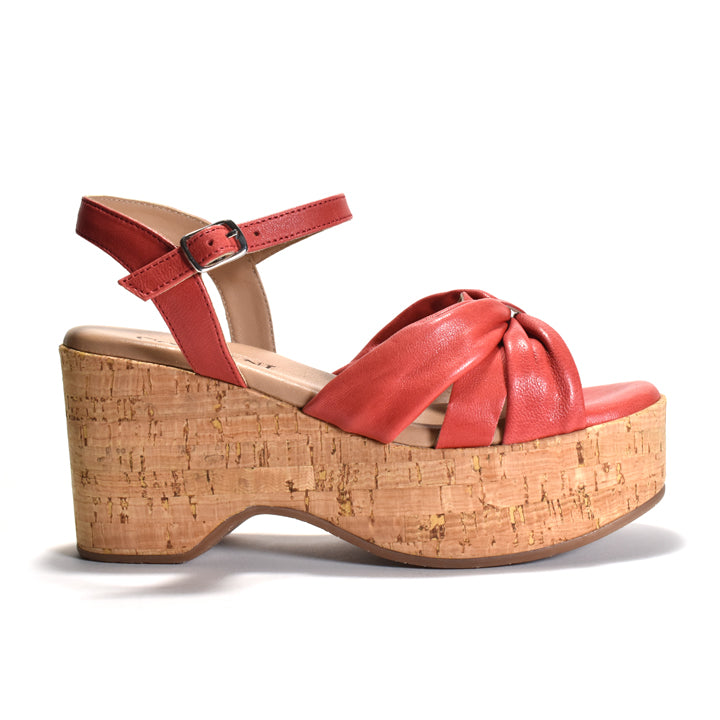 A red leather platform wedge sandal with an ankle strap and crisscross front straps, set against a plain white background.