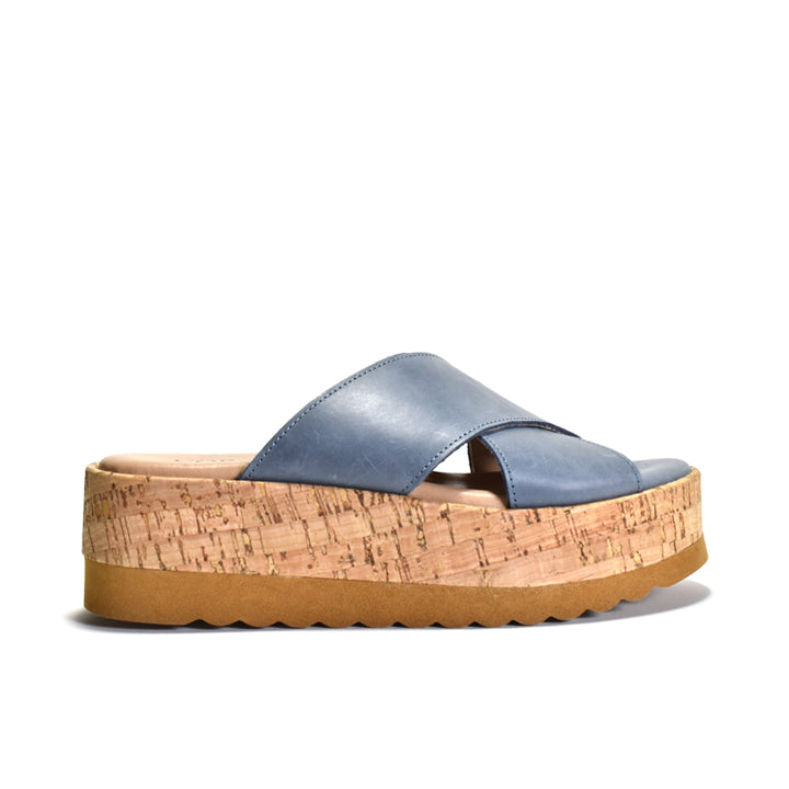 A single platform slide sandal with a dusty blue leather strap and a thick natural cork wedge sole, shown from a side profile on a white background.