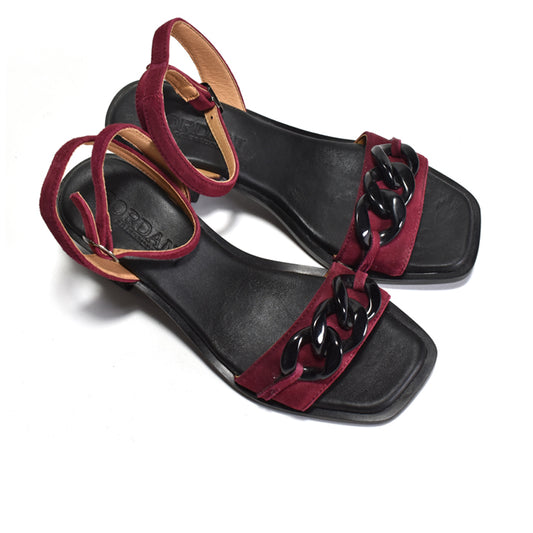 A maroon sandal with a decorative chain on a stacked black leather heel, with adjustable ankle wrap and metal buckle.