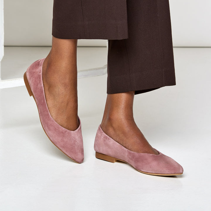 person wearing Pink suede flats worn with a dark brown pants on a light background
