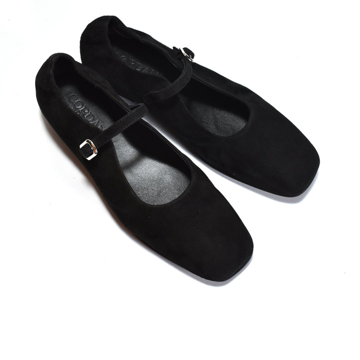 A pair of black suede flat shoes with square toes and a single strap across the instep, accented by small silver buckle details, shown on a white background.