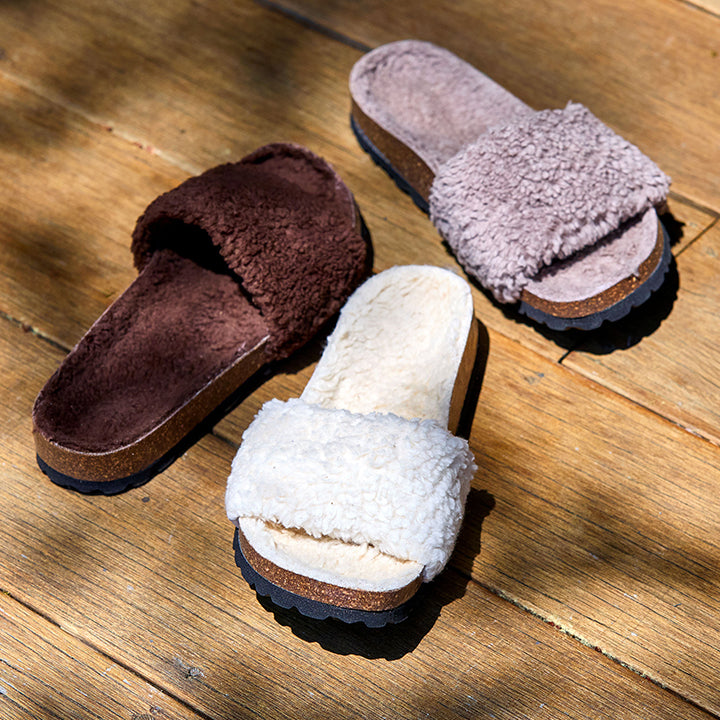 Three pairs of fluffy slippers in brown, white, and pink on a wooden floor.