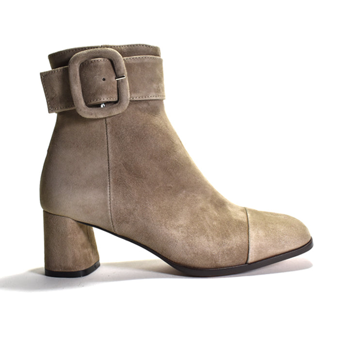 A taupe suede ankle boot with a chunky block heel, a side seam, and a wide strap with a square buckle detail on the side, shown against a plain white background.