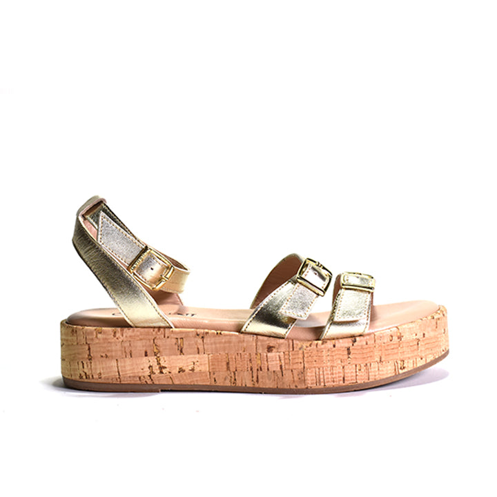 A gold two-strap sandal with adjustable metal buckles, a cork-wrapped platform, and a leather ankle strap.