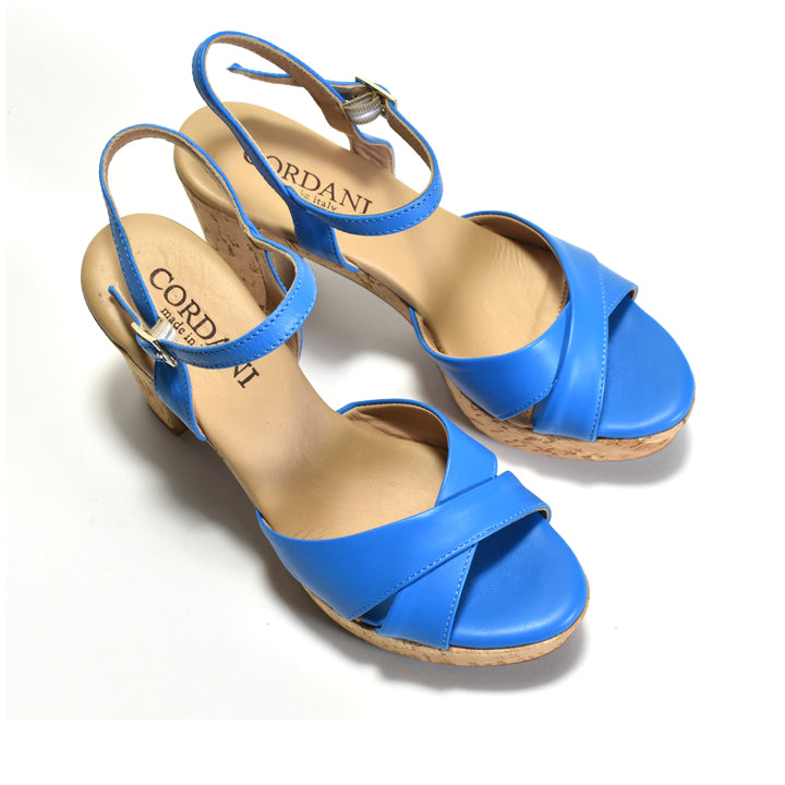 A pair of blue leather wedge sandals with crisscross straps and ankle buckles, shown on a white background. The brand name CORDANI is visible on the tan insoles.