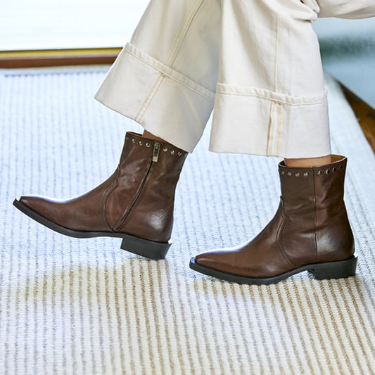 Brown leather boots worn with white pants on a textured surface