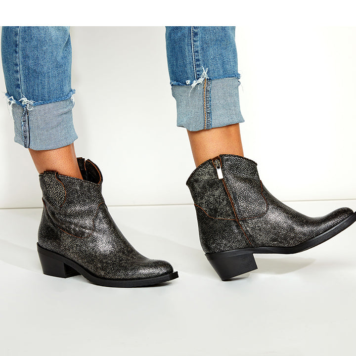 Black leather ankle boots worn with rolled-up jeans on a white background