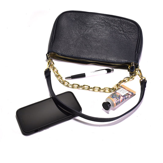 Navy handbag with gold chain strap, phone, and tube of lotion on a white background