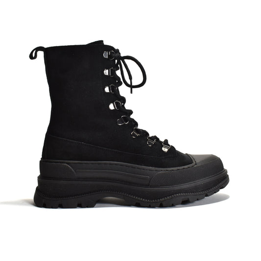 A black mid-calf lace-up boot with a thick lug sole, black suede upper, and silver metal eyelets, shown from a side profile on a white background.