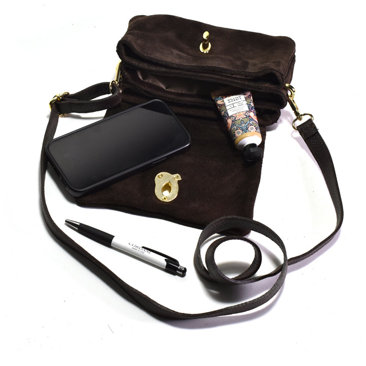 Brown handbag with black strap, phone, pen, and small item on a white background