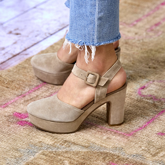 Beige suede platform shoes worn with blue jeans on a textured rug.