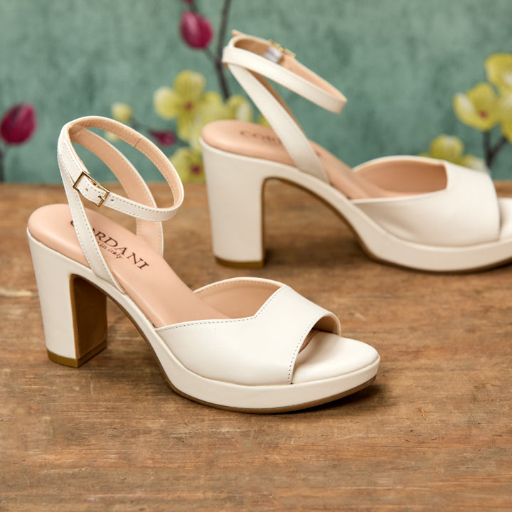 White high-heeled sandals on a wooden surface with a blurred floral background