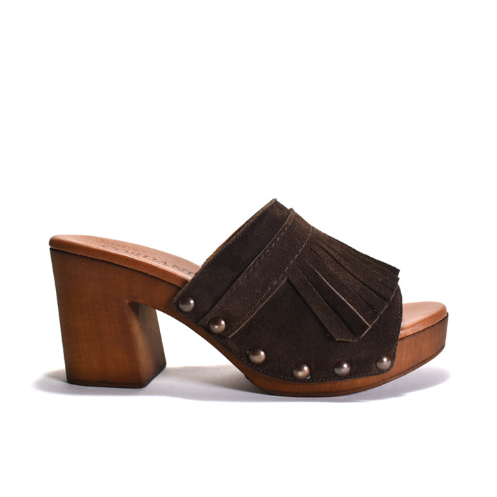A dark brown suede mule sandal with a chunky wooden block heel, platform sole, fringe detailing, and brown-tone metal studs, shown from a side profile on a white background.