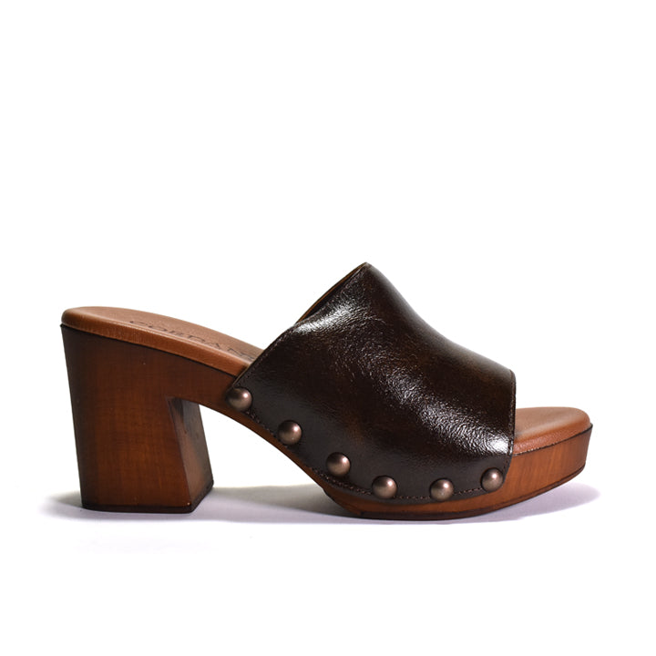 A dark brown leather mule sandal with a chunky wooden block heel, platform sole, and decorative metal studs, shown from a side profile on a white background.