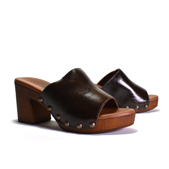 A pair of dark brown leather slide mules with wooden block heels and platforms, decorated with small metallic studs, shown on a white background.