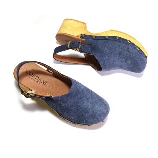 A pair of blue suede clogs with LIGHT wood-look soles and gold-tone hardware, shown on a white background. One clog is upright and the other is angled on its side, displaying the tan insole with the brand name 'CORDANI'.