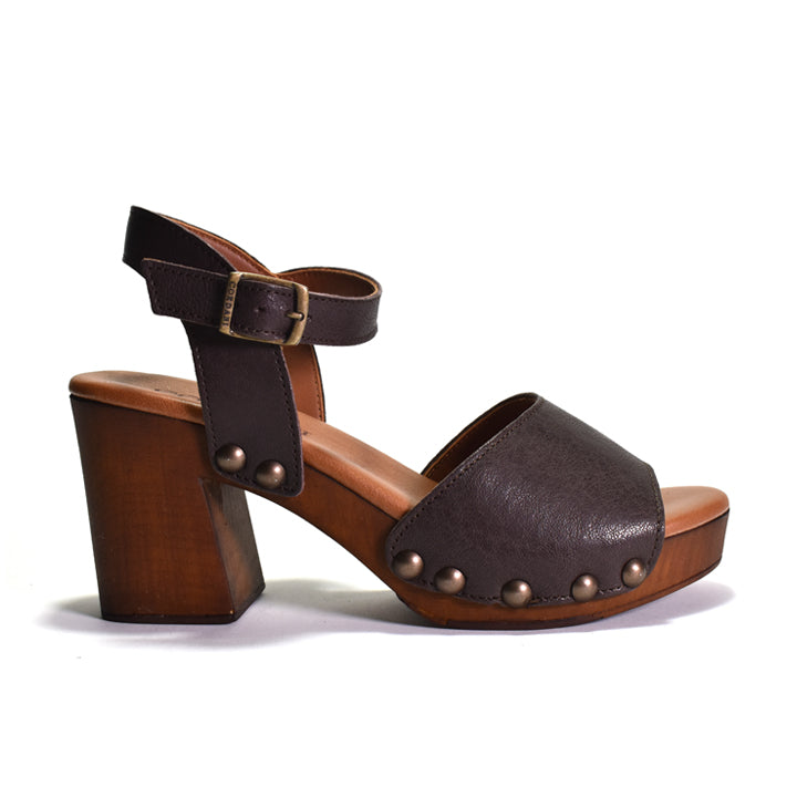 A dark brown leather platform sandal with a chunky wooden block heel, an ankle strap with a brass buckle, and decorative metal studs on the side, shown against a plain white background.