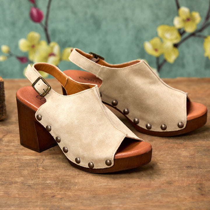 Pair of beige open-toe sandals with brown soles on a wooden surface with a floral background.