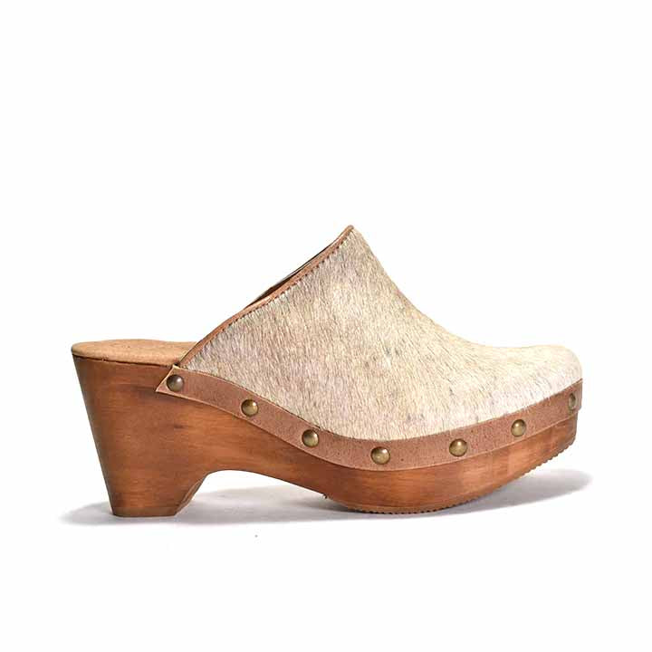 A beige cowhair clog with a light wooden heel, featuring metal eyelets 